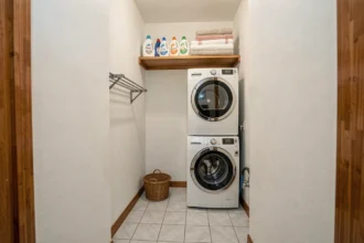 Buanderie compacte avec lave-linge et sèche-linge superposés dans une alcôve blanche, étagères en bois et panier en osier