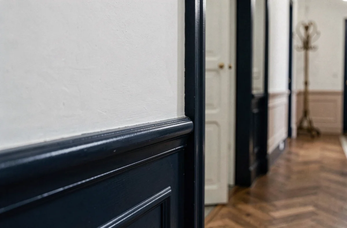 Détail de garniture bleu marine sur murs blancs dans un couloir de style haussmannien avec parquet en chevrons