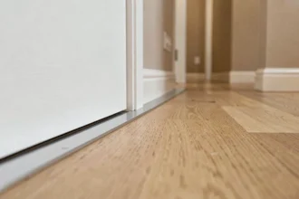 Gros plan sur le seuil de porte en aluminium entre un parquet chêne et un carrelage dans un couloir d'appartement moderne